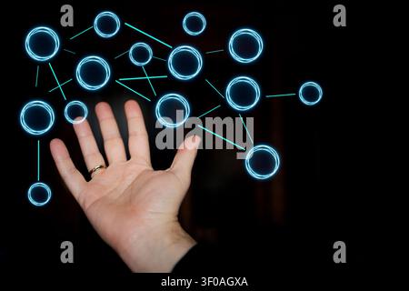 Hand extends towards illuminated blue circles and connecting lines, set against a dark backdrop, illustrating concepts of digital interaction and tech Stock Photo