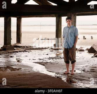 Portrait of young man standing under boardwalk on a beach Stock Photo
