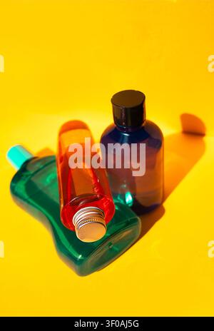 Three plastic bottles in different shapes and colors are arranged on a yellow background, featuring green, red, and blue hues with distinct caps Stock Photo