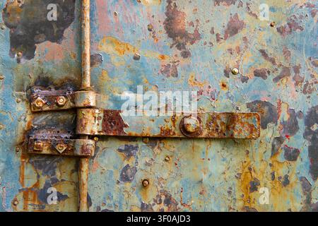A detailed texture shot focusing on a heavily rusted, oxidised iron hinge mechanism with peeling blue paint layers on a metallic container surface, hi Stock Photo