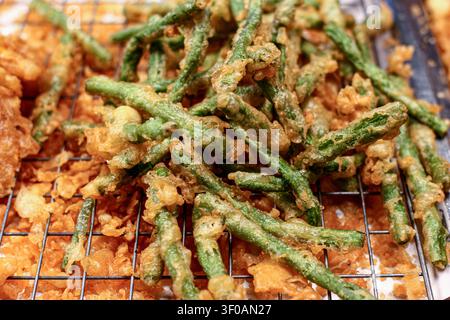 Close up of crispy fried yardlong beans coated with golden tempura batter on metal rack. Authentic Asian vegetarian snack. Stock Photo
