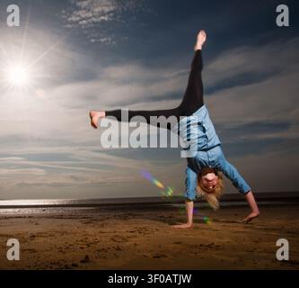 Young woman doing a cartwheel on beach at sunset Stock Photo