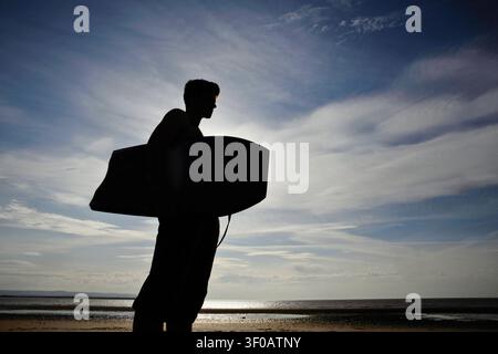 silhouette of young man with bodyboard standing on a beach looking towards the sea Stock Photo