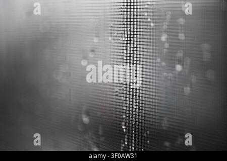Close up of a window screen covered in rain droplets creating abstract patterns Stock Photo