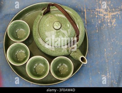 Top view of an emerald green vintage ceramic tea set with crackle glaze including a pot and cups on a blue surface with copy space. Stock Photo