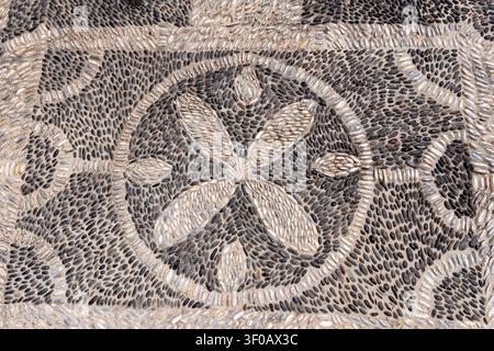 Traditional hocholaki pebble mosaic pavement on a street in Santorini. Black and white small stones arranged in a circular floral pattern create a tex Stock Photo