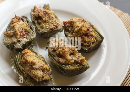 Healthy oven-roasted artichokes prepared with breadcrumbs, herbs, and garlic, served fresh on a white plate. Stock Photo