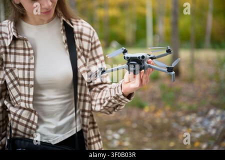 Woman holds ready drone in hand and looks at it. Close up of quadcopter outdoors, inspecting camera and design before flight, concept of hobby, preparation and technology Stock Photo