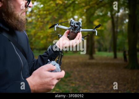 Man holds drone and prepares it for takeoff. Bearded man checking quadcopter before flight in a park, setting up equipment for aerial photography, concept of modern technology and hobby Stock Photo