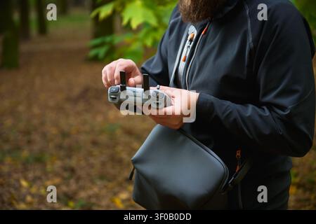 Man adjusts drone controller settings with fingers. Bearded man preparing remote control in park before flight, focusing on setup, concept of control, preparation and technology Stock Photo