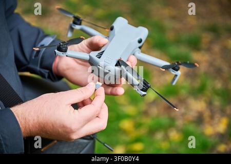Man inserts memory card into drone before flight. Close up of hands placing microSD card into quadcopter in park, preparing device for recording, concept of modern technology and aerial videography Stock Photo
