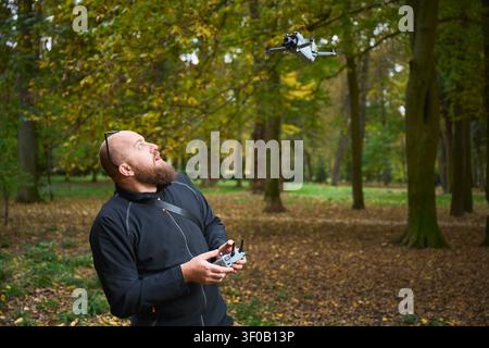 Man controlling flying drone. Bearded man operating quadcopter in park, focused on flight and reacting with excitement, concept of modern technology and hobby Stock Photo
