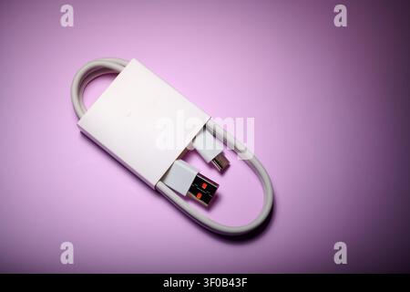 Close-up of a coiled USB-C to USB-A cable from a mobile phone on a purple surface. These cables are used for fast data transfer and charging of electr Stock Photo