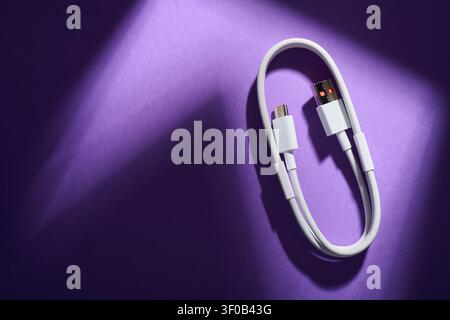 Close-up of a coiled USB-C to USB-A cable from a mobile phone on a purple surface. These cables are used for fast data transfer and charging of electr Stock Photo