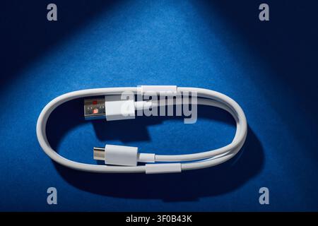 Close-up of a coiled USB-C to USB-A cable from a mobile phone on a blue surface. These cables are used for fast data transfer and charging of electron Stock Photo