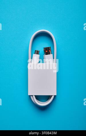 Close-up of a coiled USB-C to USB-A cable from a mobile phone on a blue surface. These cables are used for fast data transfer and charging of electron Stock Photo