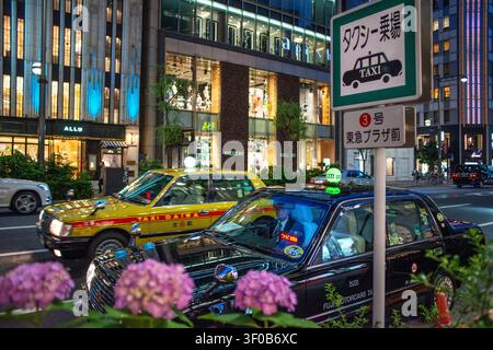 A busy taxi stand on Chuo-dori in the Ginza district is surrounded by luxury boutiques and illuminated office buildings, Tokyo, Japan.  The scene capt Stock Photo
