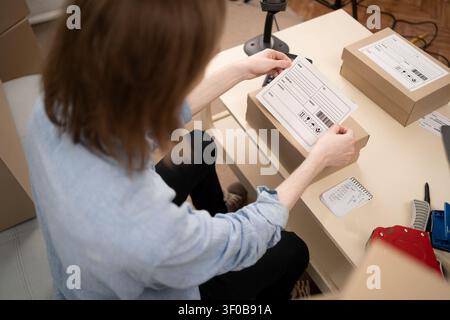 man entrepreneur fixing shipping address label on parcel in home office. ecommerce fulfillment process and preparing customer delivery. ecommerce, SME Stock Photo