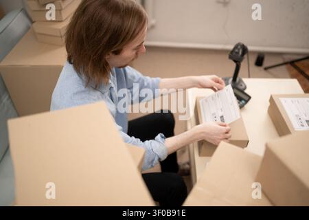 man entrepreneur fixing shipping address label on parcel in home office. ecommerce fulfillment process and preparing customer delivery. ecommerce, SME Stock Photo