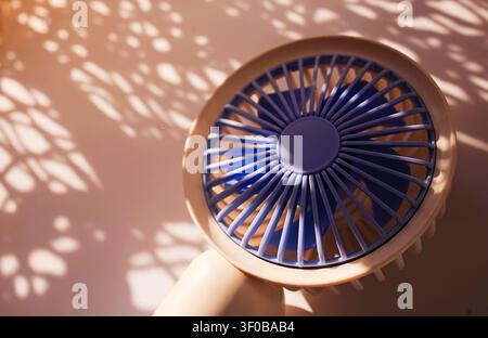 Handheld fan in blue and beige colors creates detailed shadows on a light surface, highlighting its design and structure in a well-lit setting Stock Photo