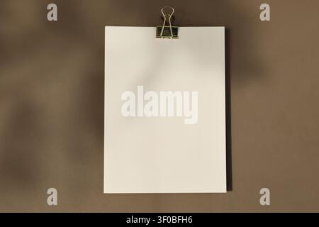 Blank White A6 A4 Paper Mockup, Golden Binder Clip on Textured Brown Background in Sunlight, Floral Shadows Overlay. Minimal Stationery Template Stock Photo