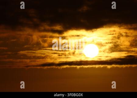 Golden evening sun shines through dramatic storm clouds, creating a glowing sky filled with warm colors, atmospheric textures and natural light. Stock Photo