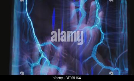 Hand touching plasma ball, creating blue electrical energy streams and static electricity Stock Photo