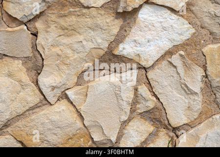 Close-up view of a rustic stone wall featuring irregular, hand-laid rocks with visible mortar lines and varied textures Stock Photo
