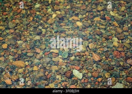 Flatland, Norway - 17.06.2026: Various sized smooth pebbles and earthy-toned stones resting under transparent, rippling water in a mountain stream Stock Photo