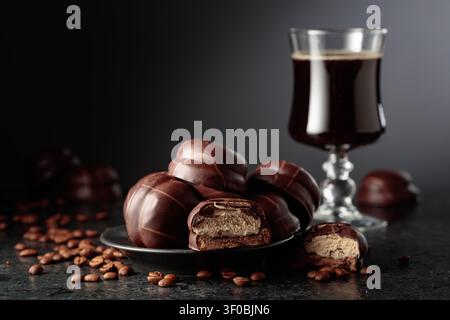 Coffee-flavoured soufflé biscuits covered in chocolate. A chocolate dessert and a cup of black coffee on a black table with scattered coffee beans. Stock Photo