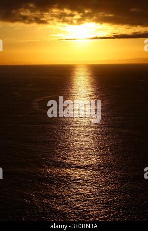 Powerful evening sunlight pierces dark clouds, creating a brilliant golden reflection across the Atlantic Ocean. A dramatic seascape showcasing the be Stock Photo