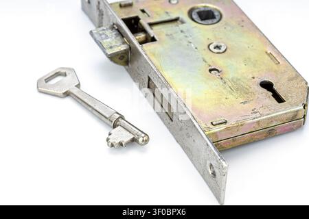 Close-up of an old vintage brass mortise door lock mechanism with an aged silver metal skeleton key lying next to it, isolated on a white background. Stock Photo
