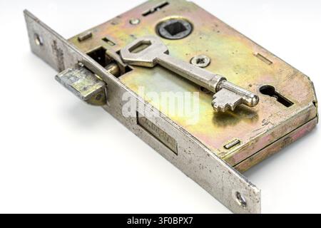 Detailed close up view of a vintage brass mortise door lock mechanism with an antique silver skeleton key resting on the iridescent metallic surface, Stock Photo