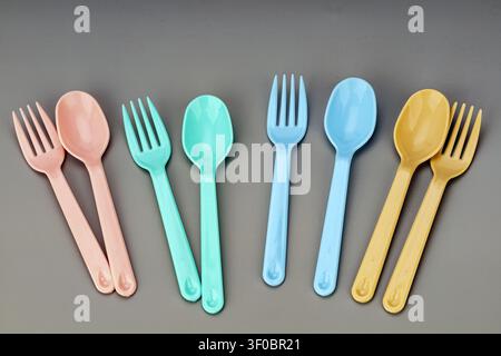 Assorted pastel colored plastic forks and spoons neatly arranged in matching pairs on modern gray background. Pink, mint green, sky blue, and yellow c Stock Photo