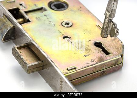 Detailed macro photograph of a vintage brass mortise door lock mechanism with a metallic skeleton key inserted into the keyhole revealing the bolt lat Stock Photo
