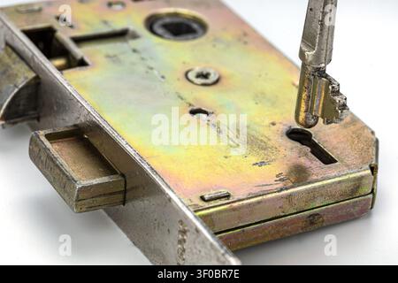 Detailed macro image of a vintage brass and steel door lock mechanism featuring an exposed latch bolt, square spindle opening, screw and worn iridesce Stock Photo