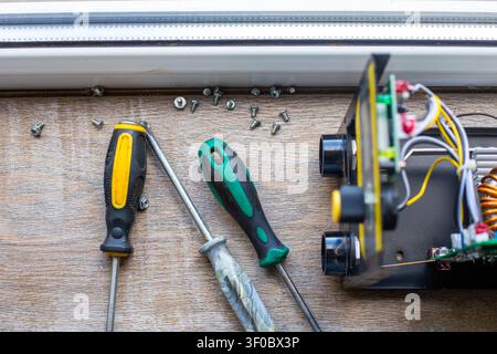 Tools and internal components of a disassembled welding inverter on a wooden surface. electronics repair, diy workshop, technical maintenance. Stock Photo