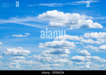 Bright white cumulus clouds drifting across vivid blue summer sky, creating peaceful natural cloudscape ideal as weather background Stock Photo