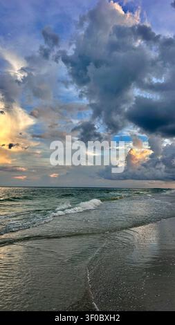 A breathtaking sunrise over the ocean with soft golden and orange light illuminating the sky and reflecting across gentle waves. Peaceful sandy beach Stock Photo