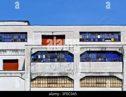 Historic 1920s functionalist warehouse facade with weathered grid windows and vibrant blue glass panes, Prague. Stock Photo