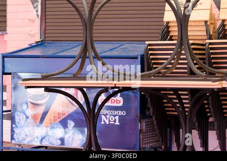 Kyiv, Ukraine - July 7, 2026: Stacked outdoor cafe tables and chairs beside a closed food kiosk in Hydropark before opening hours on a summer morning Stock Photo
