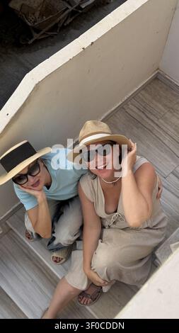 Two friends in summer outfits and sun hats are smiling and enjoying a bright day. The top-down view captures their happy expressions as they relax on Stock Photo