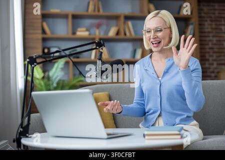Woman content creator broadcasting a live podcast or video stream, engaging with her audience online while sitting comfortably on a sofa in a modern home setup Stock Photo