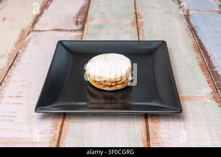 Alfajor Cookie Filled with Dulce de Leche and Dusted with Powdered Sugar on a Black Square Plate Stock Photo
