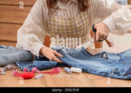 Woman cutting ripped jeans with scissors at table Stock Photo