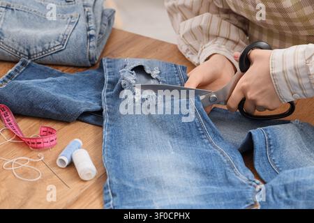 Person cutting ripped denim jeans with scissors Stock Photo