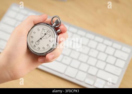 Hand holding stopwatch over computer keyboard Stock Photo