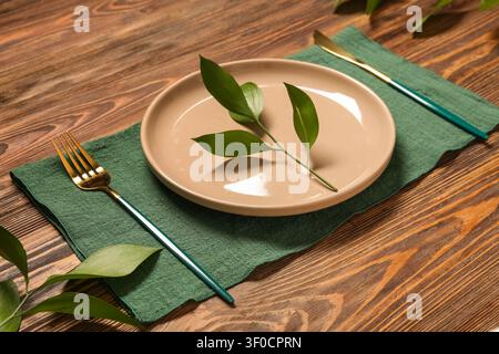 Empty beige plate with green leaves on green napkin with gold cutlery Stock Photo