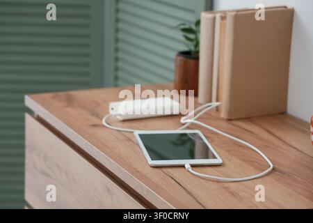 Tablet computer charging from power bank on shelf in room, closeup Stock Photo