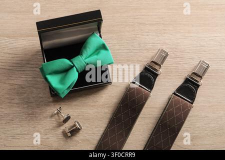 Green bow tie in box with cufflinks and suspenders on wooden surface Stock Photo